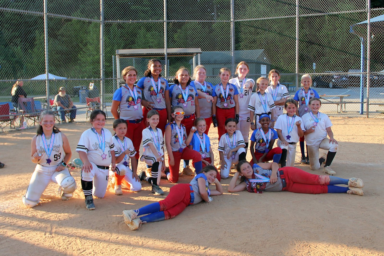 Two youth softball teams posing together on the dirt infield wearing tournament medals.
