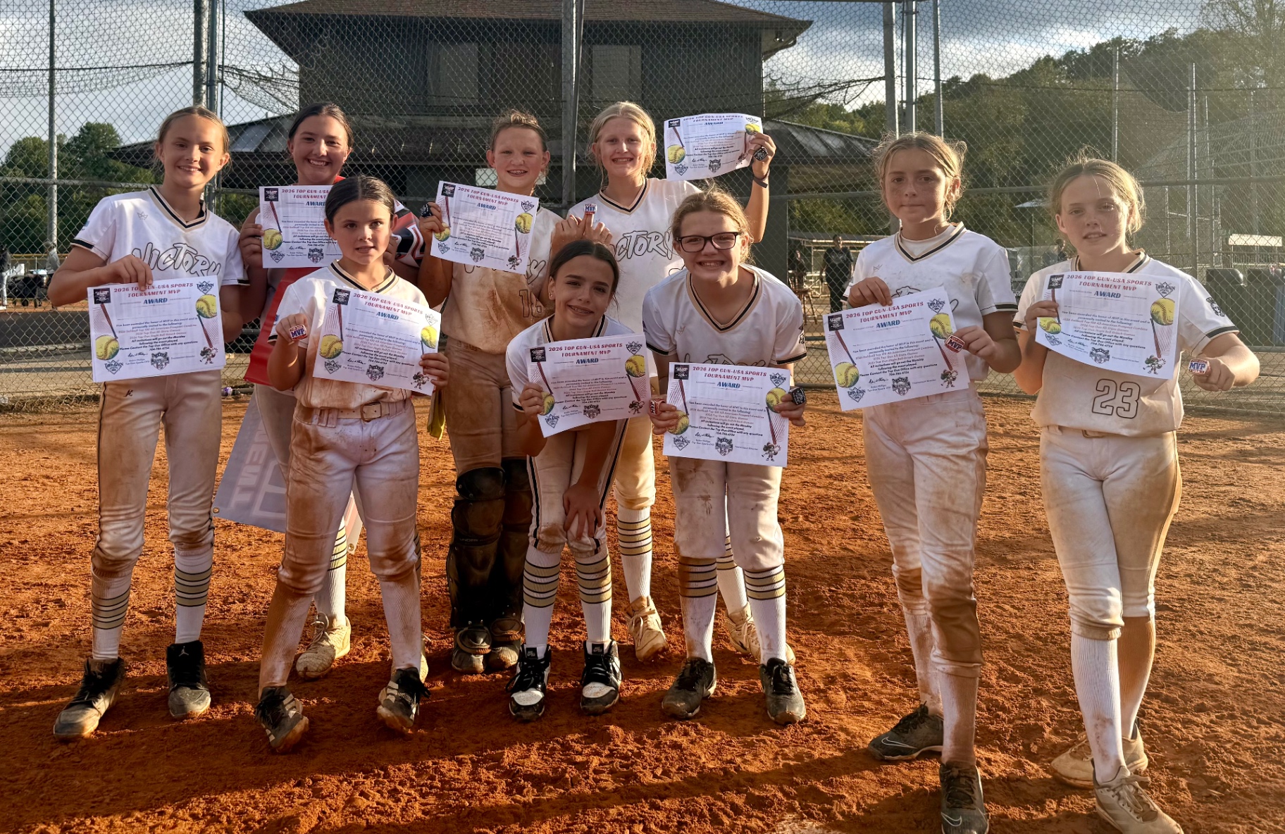 Victory softball players gathered on the field holding their 2026 Top Gun tournament MVP certificates and award rings.