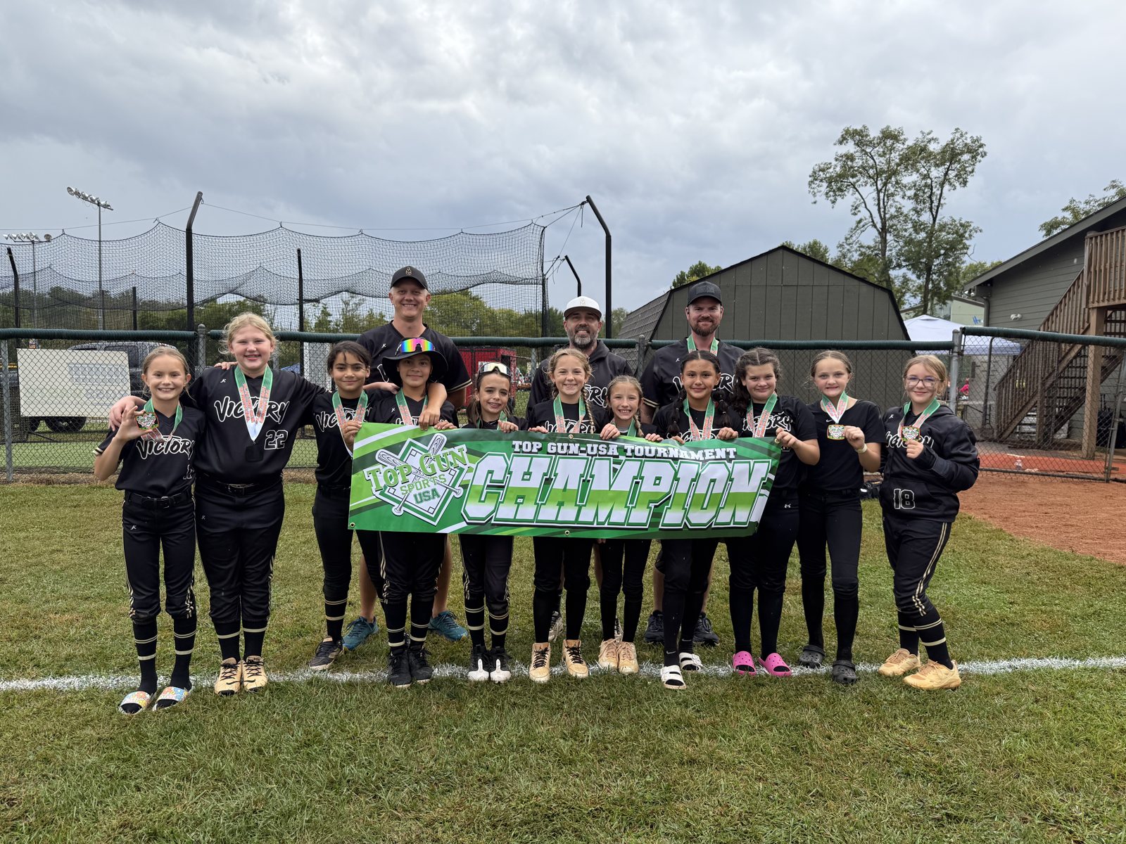 Full team and coaches lined up on grass holding a tournament banner and wearing medals.