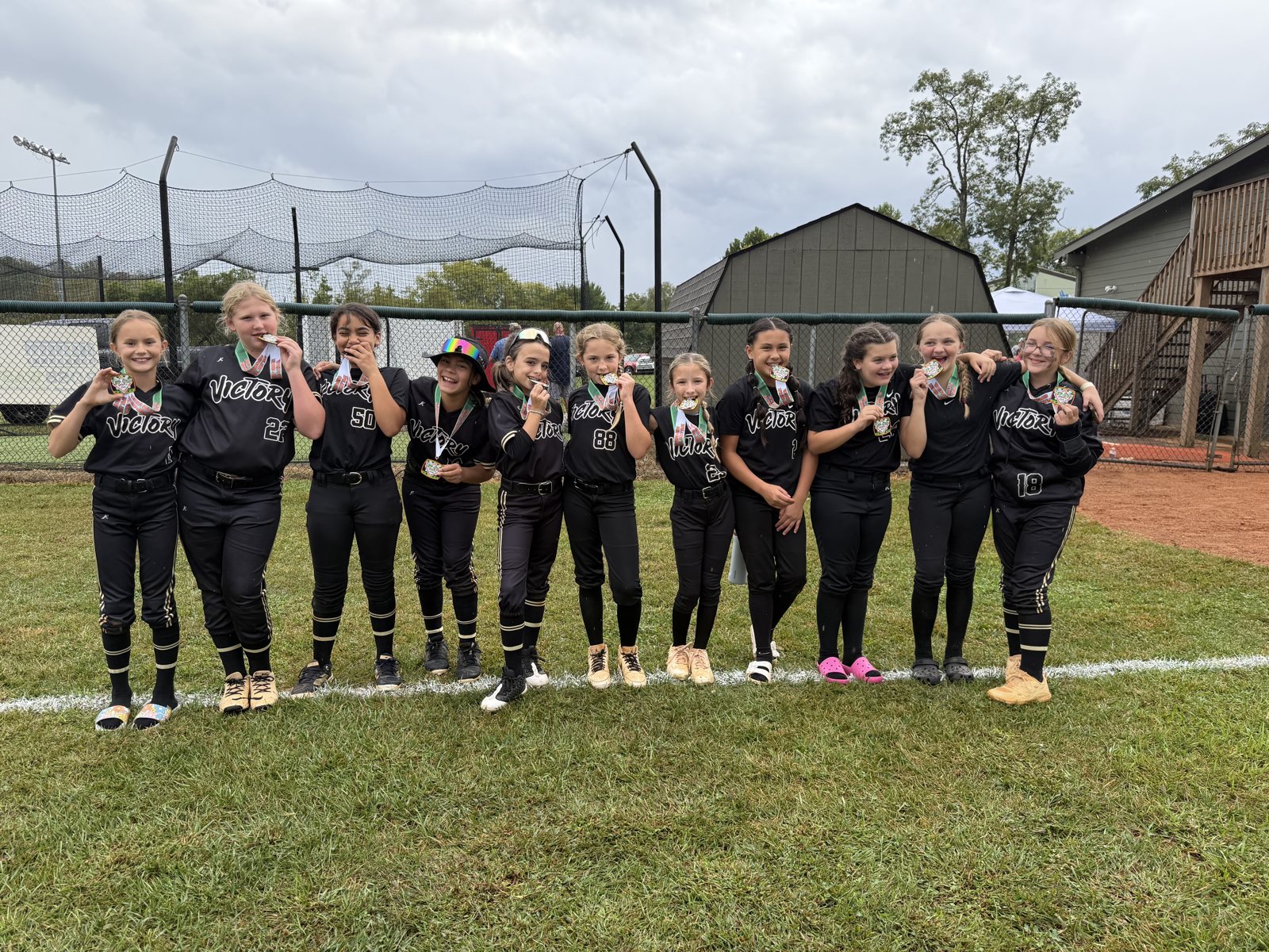 Team of softball players standing in a row on the field showing off their medals.
