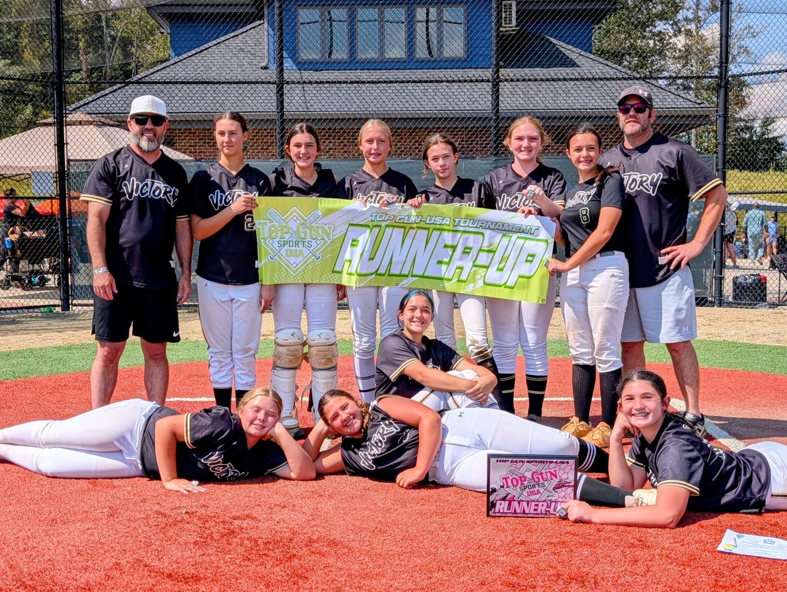 Girls travel softball team and coaches posing together on dirt with a Runner-Up banner and award plaque.