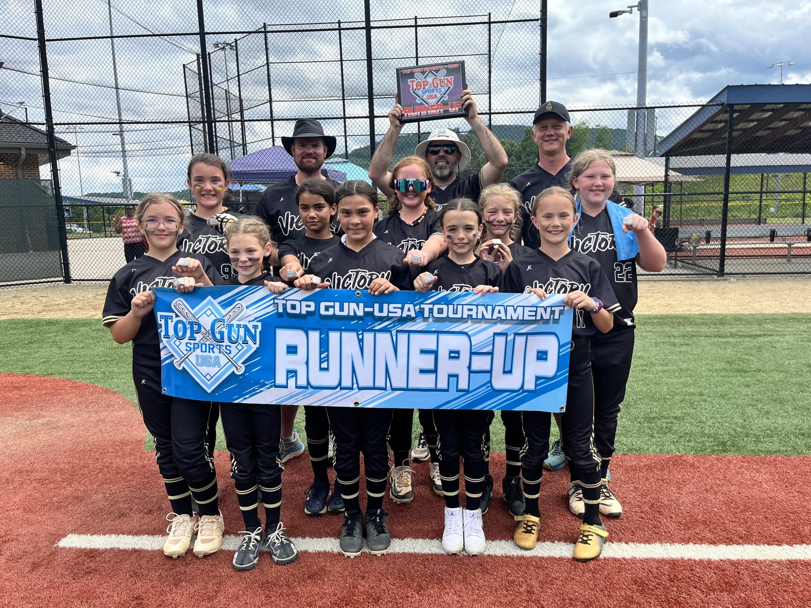 A softball team and coaches posing on artificial turf holding a Top Gun USA Tournament Runner-Up banner.