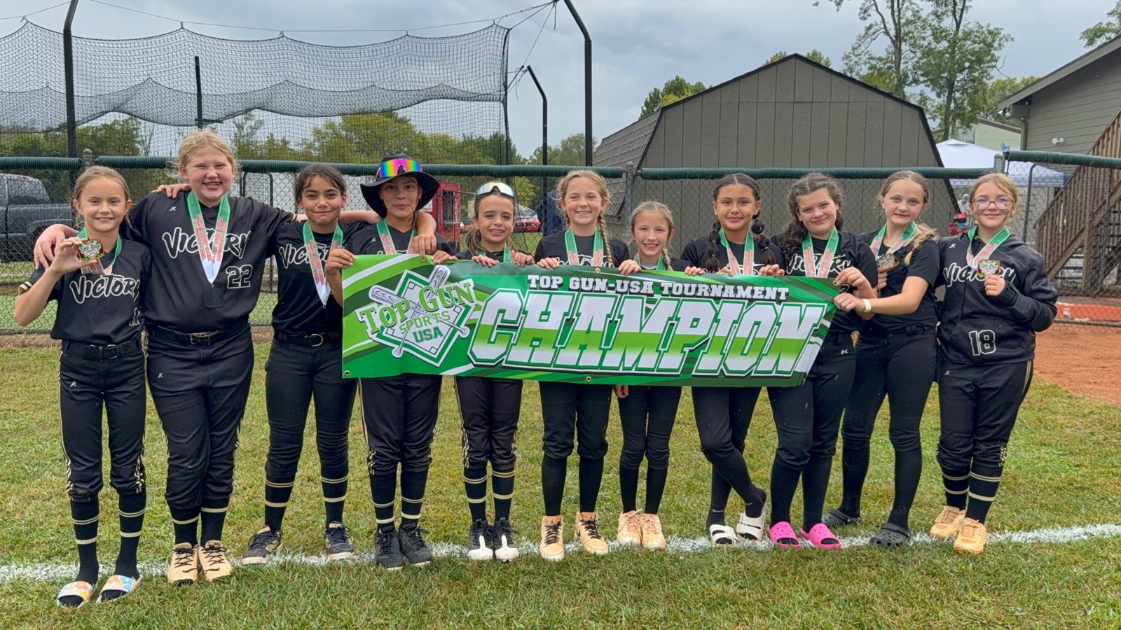 Group of softball players posing outdoors holding a green award banner and wearing medals.